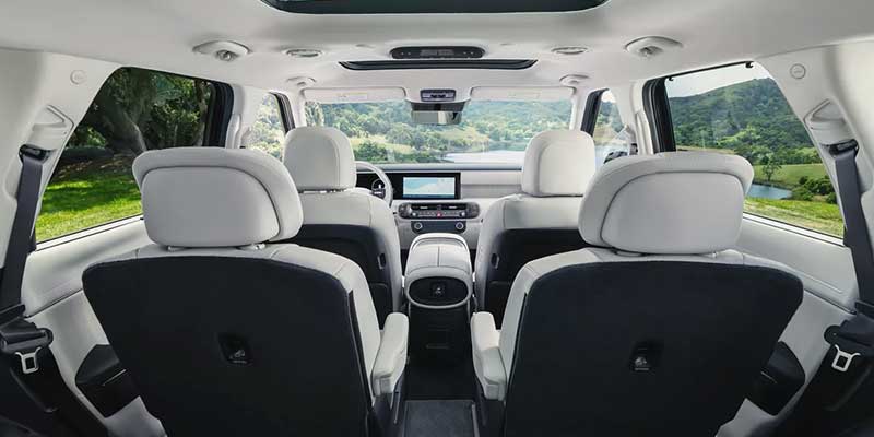 Spacious interior of the 2026 Hyundai Palisade featuring three rows of seating, light upholstery, a panoramic sunroof, and a modern dashboard with touchscreen display, viewed from the rear toward the front cabin.