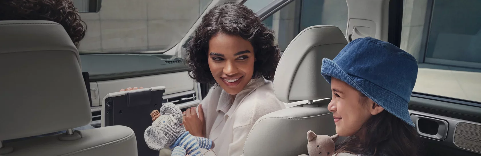 A woman and a girl sitting in a car, smiling and interacting with stuffed animals.