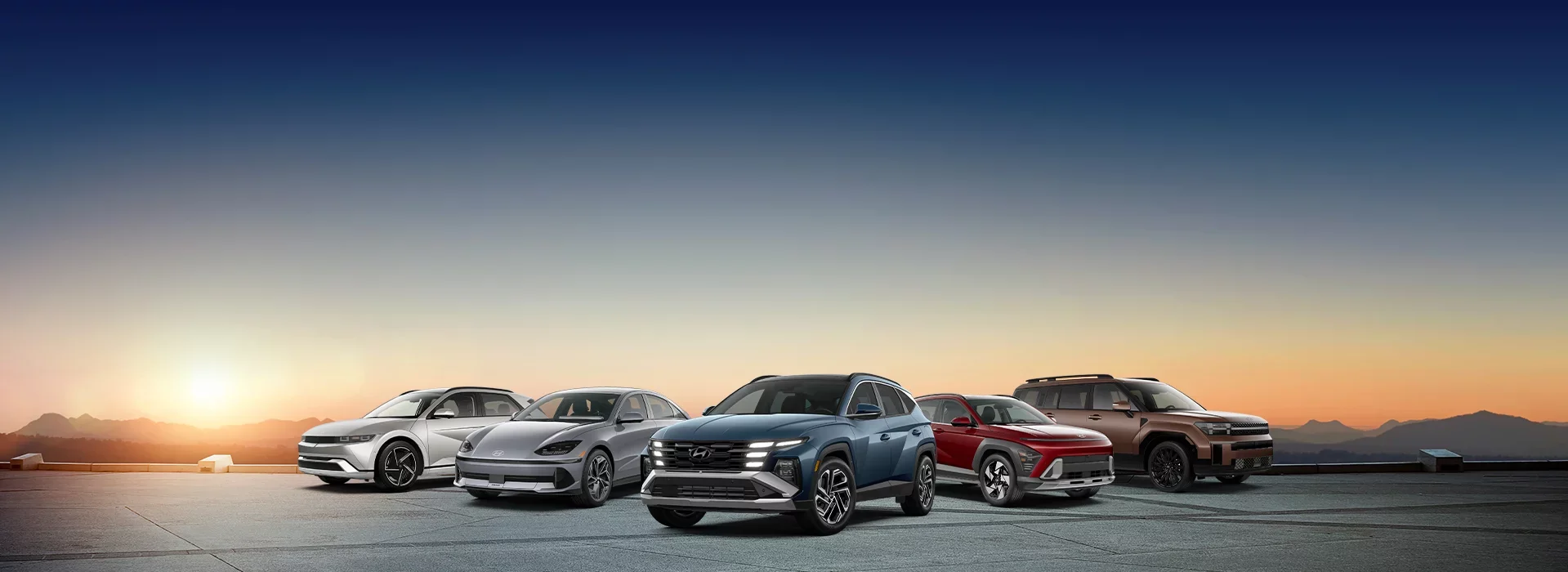 A lineup of four Hyundai cars in various colors against a sunset backdrop with mountains in the distance.