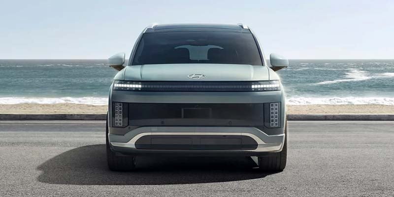 A modern Hyundai SUV parked by the ocean, showcasing a sleek front design with distinctive lighting and a minimalist grille.