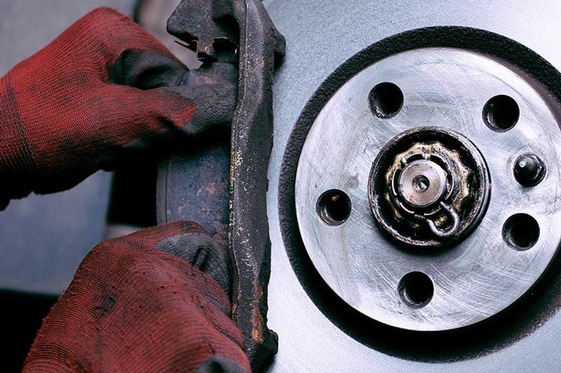 A close-up of a person wearing red gloves working on a brake system, with a brake rotor and brake caliper visible.
